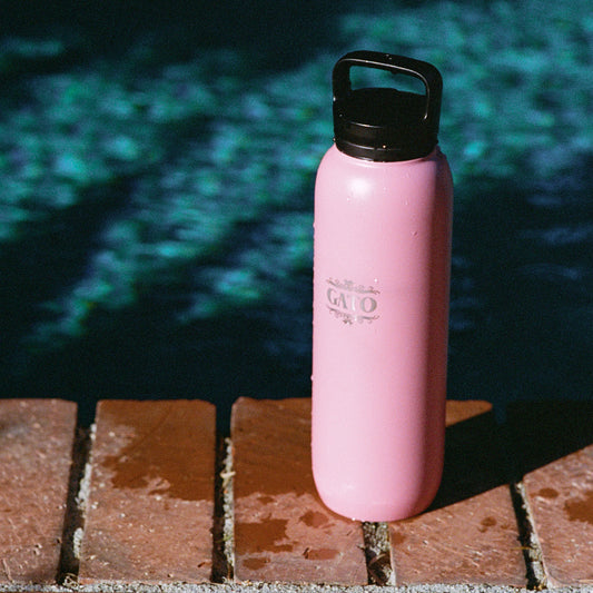 Pink water bottle with black lid on a brick surface near a pool