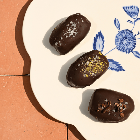 Three chocolate-dipped dates on a decorative plate with floral patterns.