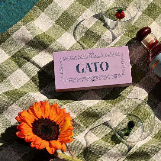 Gato product packaging on a green checkered tablecloth with a sunflower and glass.