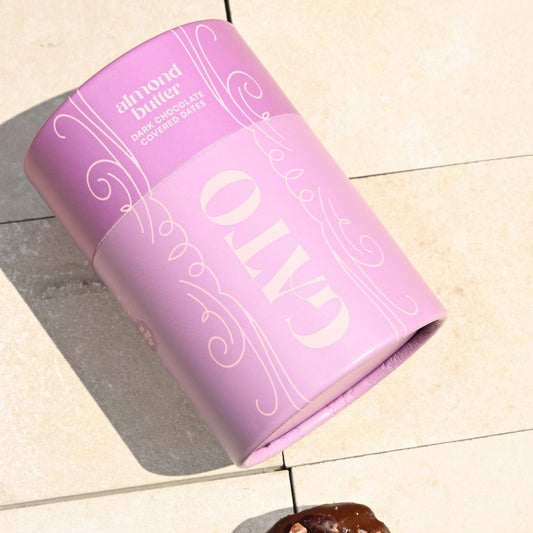 Purple cylindrical container labeled 'GATO' with a chocolate date on a tiled floor.