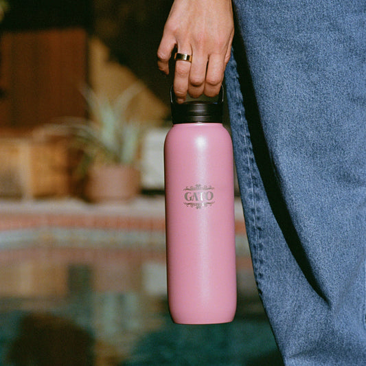 A person holding a pink stainless steel water bottle with 'GATO' branding, in front of a pool